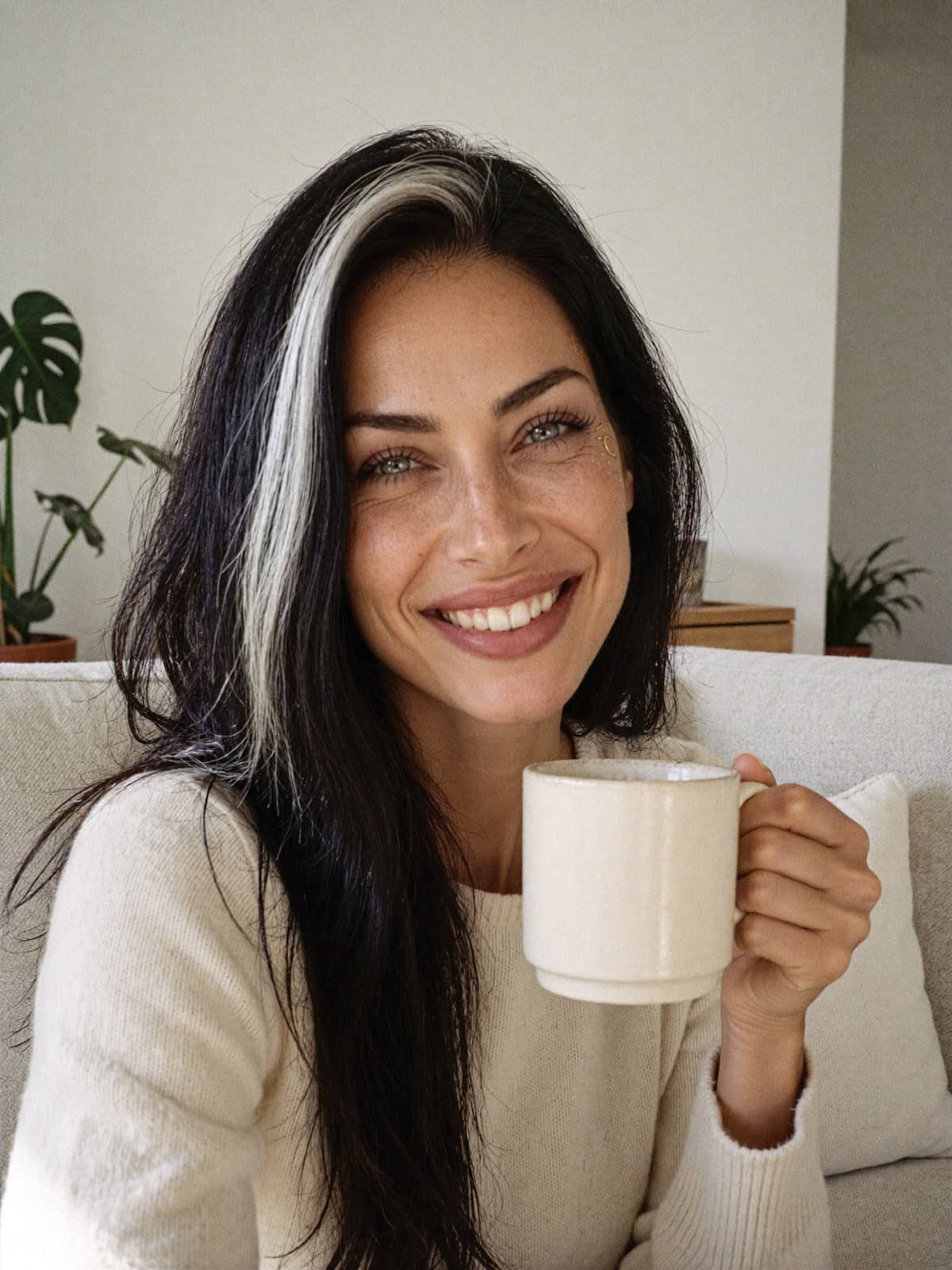 Manifelle laughing on a sofa, holding a cup of tea